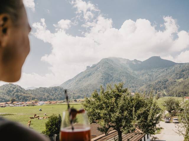 Person genießt einen Sommer-Drink auf Hotelbalkon mit Aussicht auf die Berglandschaft im Chiemgau