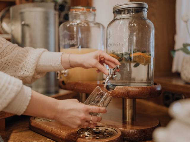 Person lässt Zitronenwasser aus einem Glasbehälter in ein Glas