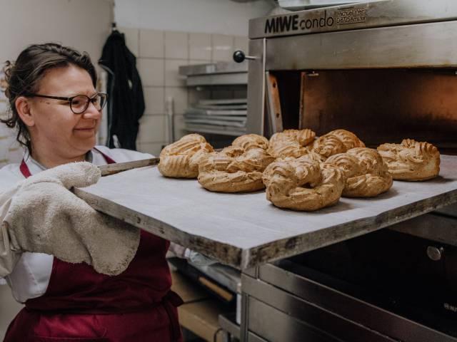 Bäckerin holt frische Brötchen aus dem Backofen