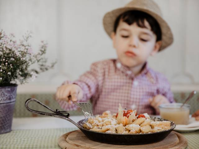 Kind mit Hund probiert frischen Kaiserschmarrn in Gusspfanne