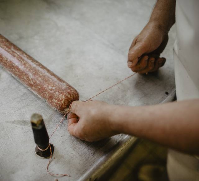 Metzger schnürt die hausgemachte Salami in der Hofmetzgerei Weßnerhof