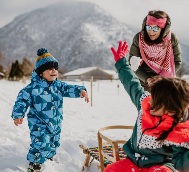 Kinder mit Mutter spielen im Schnee mit Schlitten